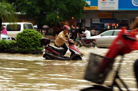 Pedestrians and vehicles wade through a flooded street in the downtown of Zhanjiang, south China's Guangdong Province, June 7, 2009. The city of Zhanjiang has been heavily inundated after being hit by a heavy rainstorm, leaving the traffic in difficulty. [Zhou Long/Xinhua]