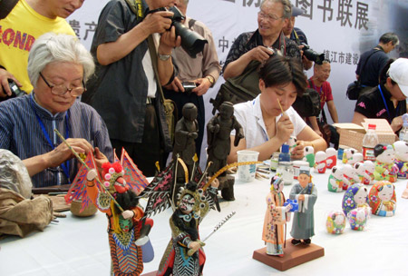 Two handicraftswomen display their skills in molding the Huishan clay-figurines, during the Traditional Chinese Folk Stunts Show, on the Xijindu Ancient Street of Zhenjiang City, east China's Jiangsu Province, June 7, 2009. [Shi Yucheng/Xinhua]