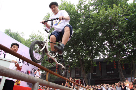 A folk stunt performer shows acrobatic skill of riding bicycle on the steel tube, during the Traditional Chinese Folk Stunts Show, on the Xijindu Ancient Street of Zhenjiang City, east China's Jiangsu Province, June 7, 2009. [Chen Gang/Xinhua]