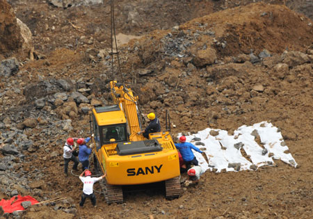 Workers help unload the excavator from a MI-26 helicopter at the landslide site in Wulong County, southwest China's Chongqing Municipality, June 11, 2009.[Liu Chan/Xinhua]