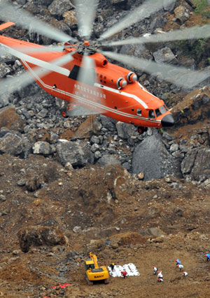 A MI-26 helicopter hovers to unload an excavator at the landslide site of Jiwei Mountain, in Wulong County, southwest China's Chongqing Municipality, June 11, 2009. The MI-26 heavy-lifting helicopter has begun carrying heavy machineries needed in the search for 63 people missing in a massive landslide on Friday. The heavy machineries will be used to remove giant rocks that buried two entrances to an iron ore mine, where 27 miners are believed to be trapped. [Liu Chan/Xinhua]