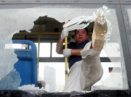 A bus company personnel breaks window open with a violent stamp during an emergency drill in Shanghai, Thursday June 11, 2009, in the wake of a freak bus blaze in southwest China's Chengdu that killed 27 passengers, leaving another 63 injured. [Xinhua]