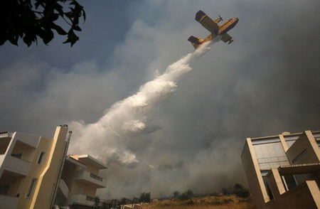 A fire-fighting airplane drops water over a bushfire at Glyfada suburb south of Athens June 15, 2009. A wildfire raged uncontrolled through forest land in the outskirts of Athens, threatening homes and power lines, a fire brigade official said on Monday. [chinanews.com] 