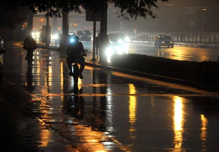 Local residents ride in heavy rain as the street lamps are turned on in downtown Beijing, China, June 16, 2009. Local authority released a yellow alert for lightings on Tuesday. [Luo Xiaoguang/Xinhua]