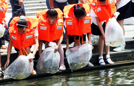 The pupils release fish fry into the water by the Chunshen Lake in Suzhou City of east China's Jiangsu Province, June 18, 2009. More than 10 million fish fry were released into the rivers and lakes within the city area of Suzhou on Thursday to improve the city's ecological environment. [Pu Jianming/Xinhua] 