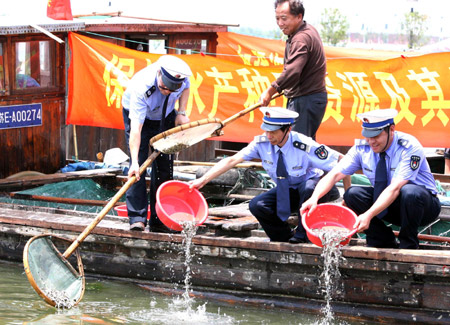 The pupils release fish fry into the water by the Chunshen Lake in Suzhou City of east China's Jiangsu Province, June 18, 2009. [Wang Jianzhong/Xinhua]