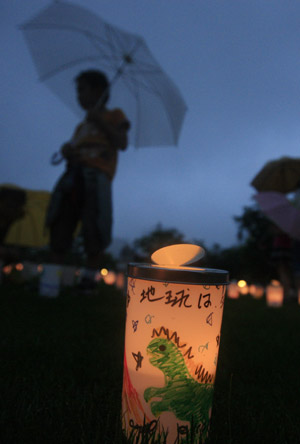 A boy passes by a plastic cup with a candle in during the Candle Night campaign to call for saving the electricity with the lights off in Roppongi in Tokyo, capital of Japan, June 21, 2009. (Xinhua/Ren Zhenglai)