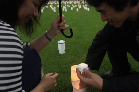 A couple lighten a candle to put it into a plastic cup during the Candle Night campaign to call for saving the electricity with the lights off in Roppongi in Tokyo, capital of Japan, June 21, 2009. (Xinhua/Ren Zhenglai)