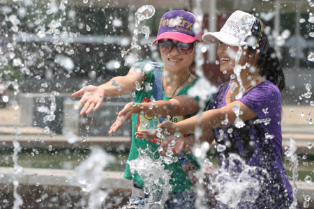 Two Chinese girls touch fountain water against a heatwave of over 35 degrees Celsius at a street square in Lianyungang City in east China's Jiangsu Province, June 25, 2009. [Xinhua]