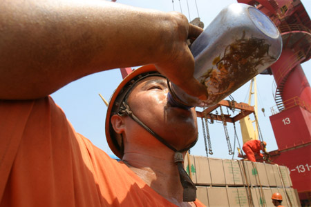 A Chinese dockworker drinks a bottle of water to quench his thirst against a heatwave of over 35 degrees Celsius at a port in Lianyungang City in east China's Jiangsu Province, June 25, 2009. [Xinhua]
