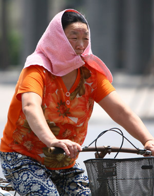 A Chinese woman, carrying a wet towel on her head to cool herself down, cycles against a heatwave of 38 degrees Celsius on a street in Fuyang City in east China's Anhui Province, June 25, 2009. [Xinhua]