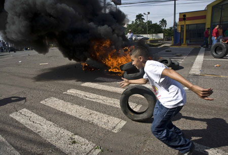 A demonstrator runs past a pile of burning tyres near the presidential house in Tegucigalpa, capital of Honduras, on June 28, 2009, during a rally calling for the release of Honduran President Manuel Zelaya. Honduran troops arrested President Manuel Zelaya in an apparent military coup Sunday to stop him pressing ahead with a constitutional referendum, in a move triggering global concern. (Xinhua/David) 