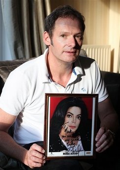 Former child star Mark Lester, who is godfather to pop star Michael Jackson's three children, poses with a photo of the star, at his home in Cheltenham, England, on Monday June 29, 2009. 