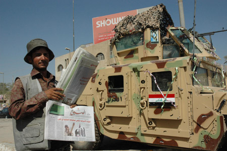 A man sells newspapers beside an Iraqi military vehicle in Baghdad, Iraq, July 1, 2009, the first day of U.S. combat troops withdrawing from major cities in Iraq. (Xinhua/Gao Shan)