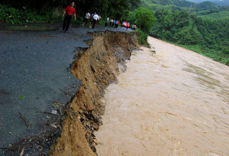 The road is eroded by the floods in Sanjiang County in southwest China's Guangxi Zhuang Autonomous Region, July 2, 2009. A heavy storm hit Gaoji Village, Heping Village, Danzhou Village etc. in Sanjiang County from Wednesday night to Thursday morning, which caused floods in these areas. The rescuing work was undergoing. [Li Shuhou/Xinhua]