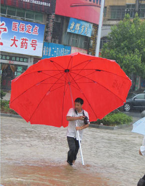 A press-photographer works in the rain on Yuanshan Avenue in Yichun City, east China's Jiangxi Province, July 2, 2009. A storm hit Yichun City from Tuesday to Thursday. [Xinhua]