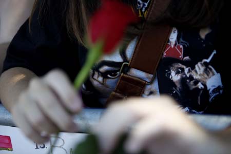 A fan wearing a Michael Jackson t-shirt holds a rose by a memorial for the deceased pop star outside the Jackson family home in Encino, California July 3, 2009.