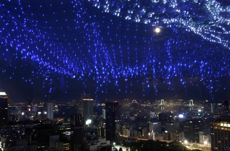 A light display of the Milky Way is reflected on a window as skyscrapers and the Tokyo Bay area are seen in background from a viewing deck of Tokyo Tower July 5, 2009. The Milky Way Illuminationis made up of 10,000 blinking blue lights to resemble the Milky Way. [Xinhua/Reuters]