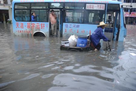 A local tricyclist struggles his way in the flood with a shut-down bus being detained nearby in downtown Yingtan city in southern China's Jiangxi Province, July 4, 2009. Heavy rain and storm struck the city Saturday paralysing part of the city's communications. [Hu Nan/Xinhua]