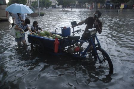 A local tricyclist struggles his way in the flood with the help of passersby in downtown Yingtan city in southern China's Jiangxi Province, July 4, 2009. Heavy rain and storm struck the city Saturday paralysing part of the city's communications. [Hu Nan/Xinhua]