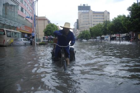 A local tricyclist struggles his way at the flooded street in downtown Yingtan city in southern China's Jiangxi Province, July 4, 2009. Heavy rain and storm struck the city Saturday paralysing part of the city's communications. [Hu Nan/Xinhua]