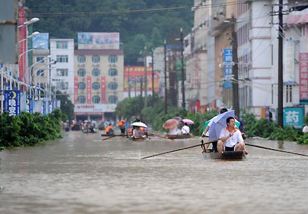 Local people paddle boats on a flooded street in Rongshui Yao Autonomous County, southwest China's Guangxi Zhuang Autonomous Region, July 4, 2009. Floods caused by rainstorms since early the week have left four people missing and 11,845 others displaced in Guangxi. The torrential rains have also damaged 12,440 hectares of crops and killed 53,300 heads of cattle. [Xinhua/Zhou Hua] 