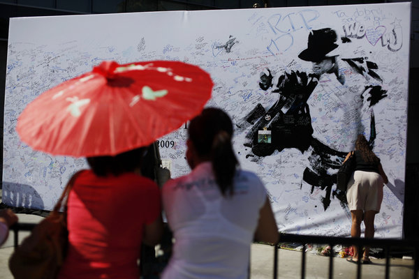 Ana Marie, left, and her sister Aileen De Leon, both of Los Angeles view a large poster at the Staples Center in Los Angeles, Sunday, July 5, 2009. The venue is the planned location for late pop star Michael Jackson's memorial service scheduled for Tuesday, July 7.