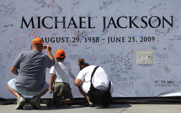 Michael Navarro, left, Michael Navarro, Jr., 7, center, and Gina Rodriguez, all from Los Angeles, sign and photograph a large poster at the Staples Center in Los Angeles, Saturday, July 4, 2009, which will be the site for the late pop star Michael Jackson's memorial service taking place Tuesday, July 7, 2009. 
