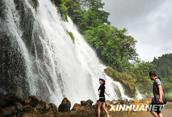 Two tourists play beside a waterfall in Libo Small Seven Holes Scenic area in Guizhou province, in a photo published on Sunday, July 5, 2009. [Photo: Xinhuanet.com]