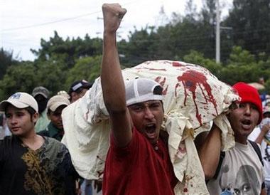 Supporters of Honduras' ousted President Manuel Zelaya gesture as they carry a sheet stained red paint, representing blood, during a protest near the presidential residence in Tegucigalpa, Monday July 6, 2009. [Esteban Felix/AP Photo] 