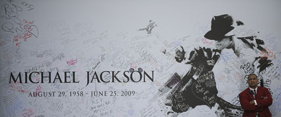 A man stands in front of the theme board for Michael Jackson public memorial outside the Staples Center in Los Angeles on July 7, 2009. A star-studded public tribute to Michael Jackson was held here Tuesday with thousands of randomly selected fans joining family and friends to bid farewell to the King of Pop. 
