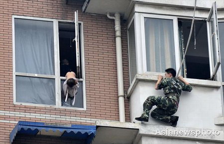 A firefighter tries to approach a two-year-old when her father who allegedly took drugs attempts to commit suicide with his kid by jumping from a window in Chengdu, Sichuan province on Tuesday, July 7, 2009. [Asianewsphoto] 