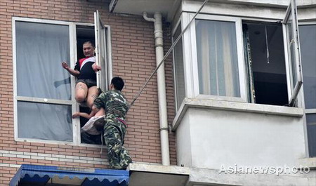 A firefighter tries to close the window to prevent a man who attempts to commit suicide with his daughter from jumping in Chengdu, Sichuan province on July 7,2009. [Asianewsphoto] 
