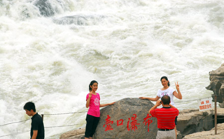 Two visitors take photo at the scenic spot of the Hukou Waterfall on the Yellow River in Jixian County, north China's Shanxi Province, July 7, 2009. Due to less rainfalls in the upper reaches of Yellow River that lessens the velocity of river flows to churn up and drive forward the sand sediments, water of the waterfall became clear.[Yan Ruipeng/Xinhua] 