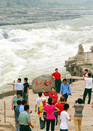 Visitors have photos taken at the scenic spot of the Hukou Waterfall on the Yellow River at Jixian County, north China's Shanxi Province, July 7, 2009.[Yan Ruipeng/Xinhua]