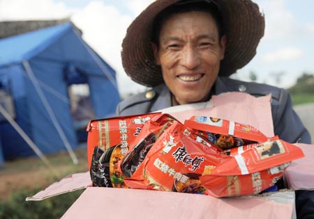 A villager of Yi ethnic group receives a box of instant noodles at Mayou Village in Guantun Township of Yao'an County, southwest China's Yunnan Province, July 12, 2009. Now more than 20,000 earthquake victims have been placed in tents and have received basic relief materials. (Xinhua/Lin Yiguang) 