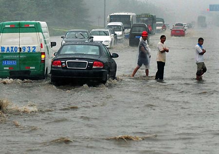 Vehicles run at a flooded street in Zhengzhou, capital of central China's Henan Province, July 13, 2009. A heavy rain hit the city early Monday and a blue alarm had been announced. [Wang Song/Xinhua]