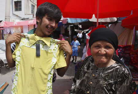 A vendor displays clothes to a woman at a bazaar in Yining, northwest China&apos;s Xinjiang Uygur Autonomous Region, July 12, 2009. Local residents of various ethnic groups went to bazaars, their traditional markets, for shopping on Sunday. (Xinhua/He Junchang) 