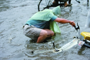 A man riding an electric bicycle falls onto a flooded road in Beijing on Monday, July 13, 2009. [The Beijing News]