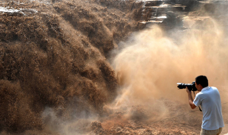 A photographer takes photos of the Hukou Waterfall of the Yellow River in northwest China's Shaanxi Province, July 18, 2009. Recent rainfalls on the upper reaches of the Yellow River have brought a heavy load of sediment in the form of sand and mud, making the water yellower than usual. [Xinhua]