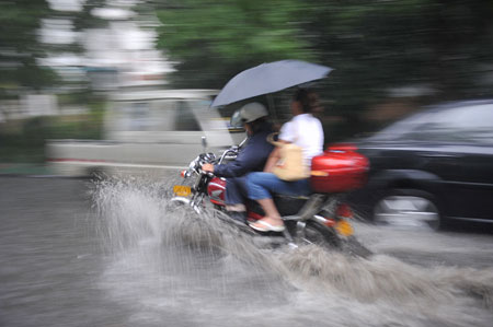 A motor cycle and cars drive on a flooded street as a heavy rain hits Hefei, capital city of east China's Anhui Province, July 23, 2009. [Yang Xiaoyuan/Xinhua]