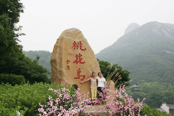 Two women pose for a photo in front of a huge rock engraved with the name of Taohua Island in Chinese on July 23, 2009. [Photo: CRIENGLISH.com] 