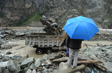 A person watches an excavator working at the site of the landslide in Kangding, southwest China's Sichuan Province, July 26, 2009. [Jiang Hongjing/Xinhua]