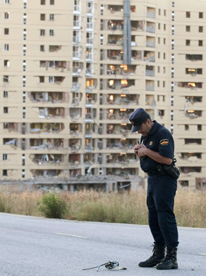 A policeman looks down at a piece of debris in front of a civil guard barracks after a car bomb exploded in the northern Spanish city of Burgos, early July 29, 2009.[Xinhua/Reuters]