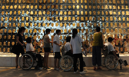 Survivors of the Sichuan earthquake on May 12, 2008 view the 'mourning wall' installed with looks of the victims at the fourth Chengdu Biennial Exhibition in Chengdu, capital of southwest China's Sichuan Province, July 29, 2009. The exhibition, kicked off on July 28 with theme of 'Narrate China', showed off 271 works by 122 artists from home and abroad. [Jiang Hongjing/Xinhua] 