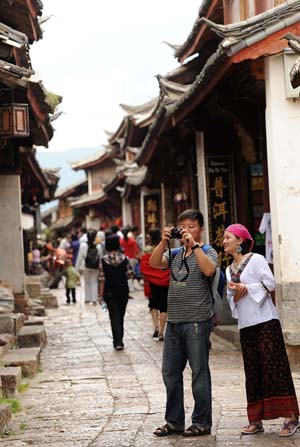 Tourists take photos on a street in Lijiang, southwest China's Yunnan Province, on July 29, 2009. More than 3.4 million tourists visited Lijiang, located on the northwest tip of Yunnan, in the first half of 2009, increasing 26 percent from the same period of 2008. Lijiang with an 800-year history was listed by the UNESCO in 1997 as a world cultural heritage site. [Lin Yiguang/Xinhua]