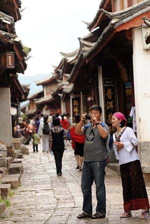 Tourists take photos on a street in Lijiang, southwest China's Yunnan Province, on July 29, 2009. More than 3.4 million tourists visited Lijiang, located on the northwest tip of Yunnan, in the first half of 2009, increasing 26 percent from the same period of 2008. Lijiang with an 800-year history was listed by the UNESCO in 1997 as a world cultural heritage site. (Xinhua/Lin Yiguang)