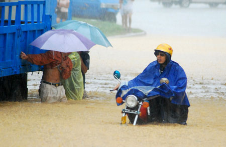 A man pushes his motorcycle past a stranded truck on a flooded street as a heavy rainstorm hits Jiujiang city in east China's Jiangxi Province, July 29, 2009. Local emergency department employees of the city are on standby to answer emergent calls as some local streets were flooded. 