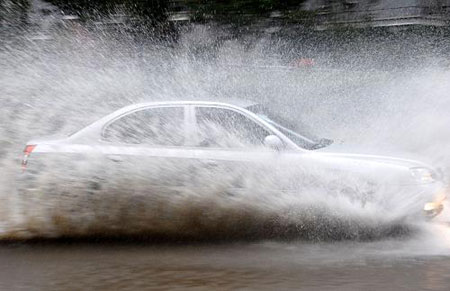 A car runs past a section of a flooded street in Shanghai, China, July 30, 2009. A short-time storm hit Shanghai due to a heavy cloud cluster on Thursday. Local observatory issued red alert signal of rain storm. The heaviest rains in 70 years hit China's largest city, Shanghai, Thursday, flooding 3,000 households and more than 70 roads. [Xinhua]