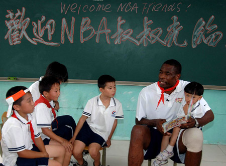 NBA player Dikembe Mutombo (R) helps students of a primary school of rural migrant workers' children to practise English during the 2009 Basketball Without Borders Asia tour in Beijing, capital of China, July 30, 2009. NBA players donated computers to this school and helped build a basketball pitch before their visit. [Gong Lei/Xinhua] 